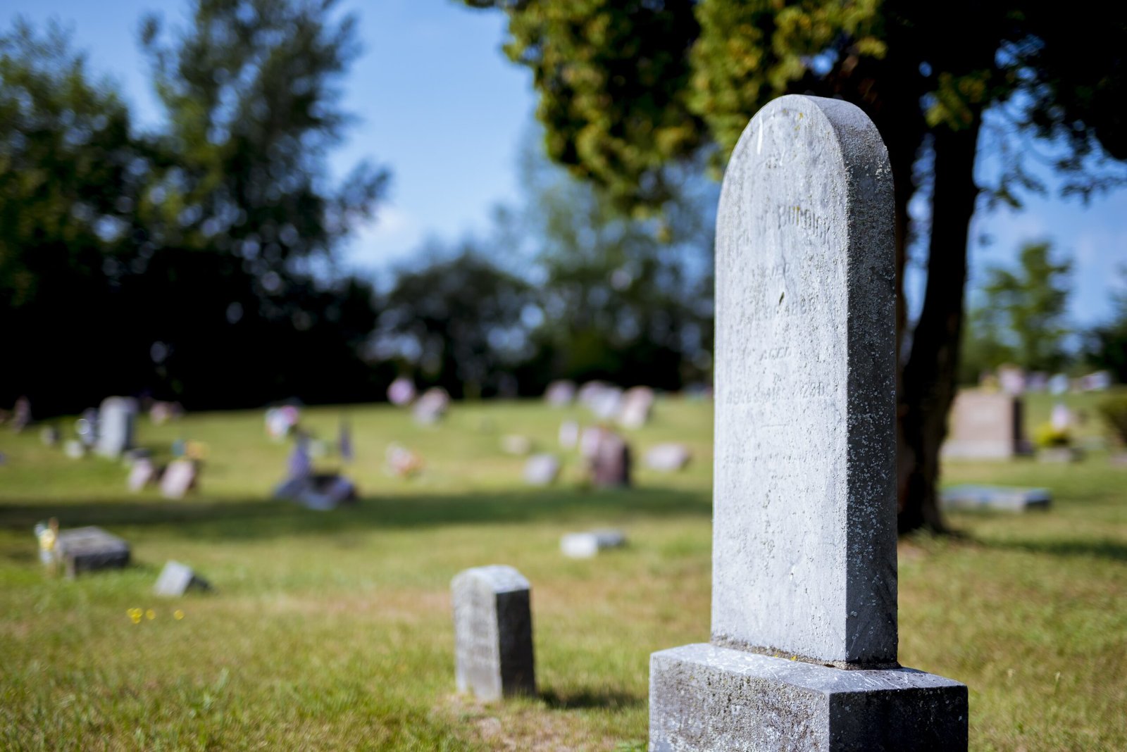 Closeup Shot Of A Gravestone With A Blurred Background At Daytime Closeup Shot Of A Gravestone With A Blurred Background At Daytime